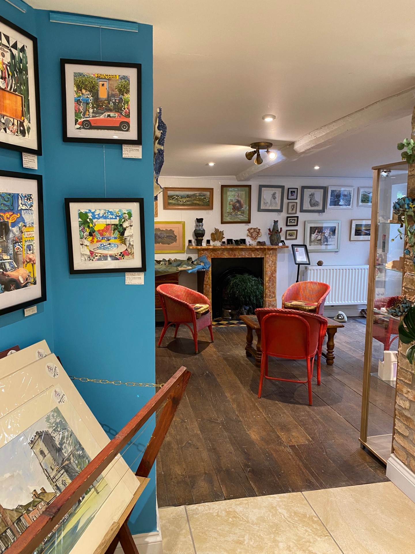 An art gallery has walls painted in blue and white. Art work is hung on all the walls and a seating area is in front of a fireplace.