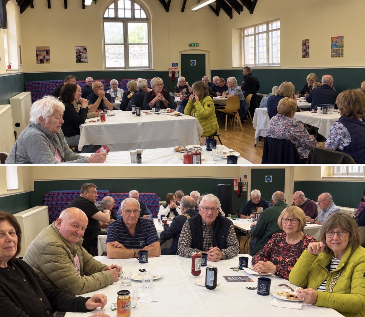A Community Hall is filled with long dining tables filled with groups of people eating.